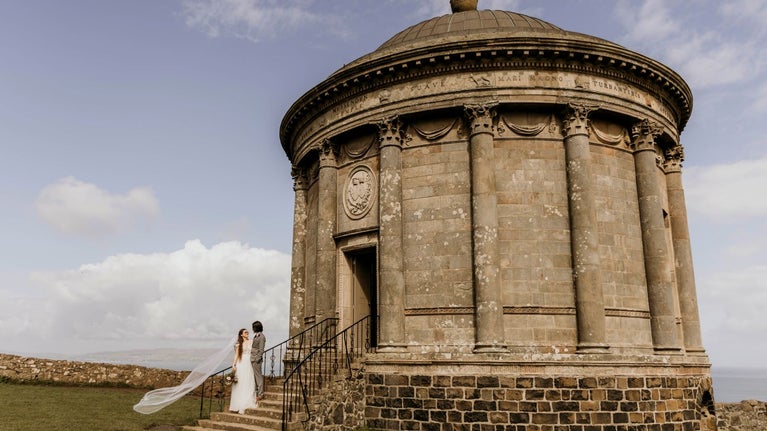 An image of a bride and groom standing on the steps of Mussenden Temple.